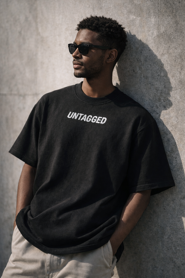 Man wearing a black 'UNTAGGED' t-shirt against a gray wall.