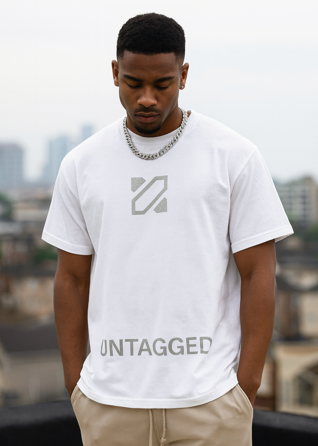 Man wearing a white t-shirt with a logo and text, standing against an urban background.