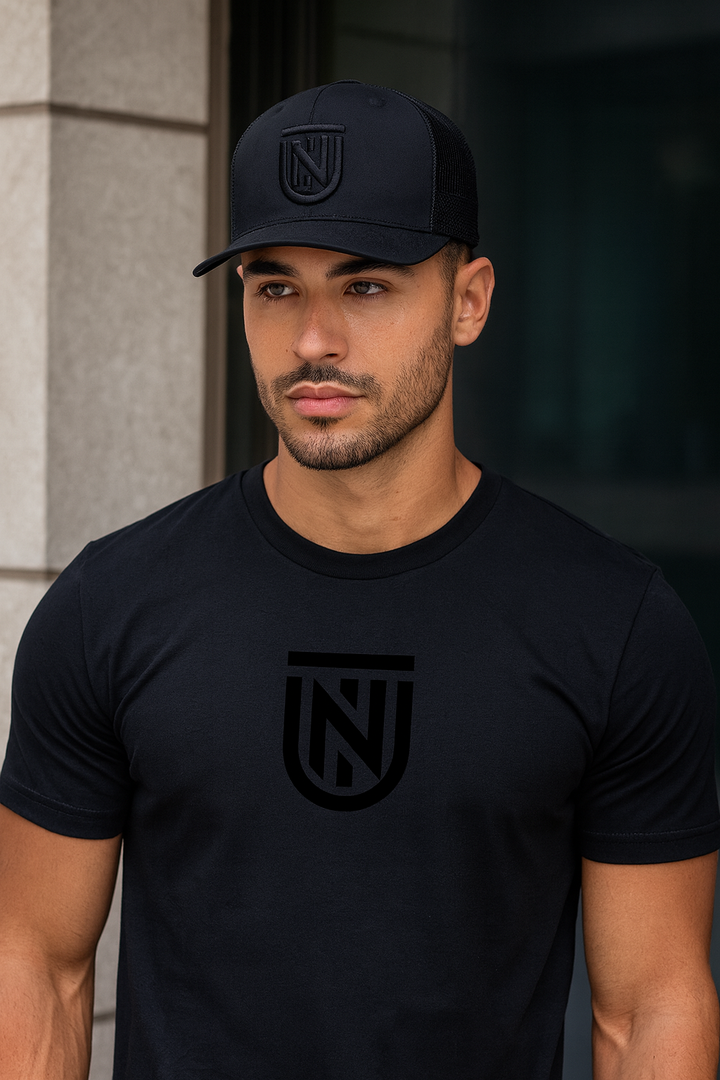 Man wearing a black t-shirt and cap with a logo, standing against a neutral background