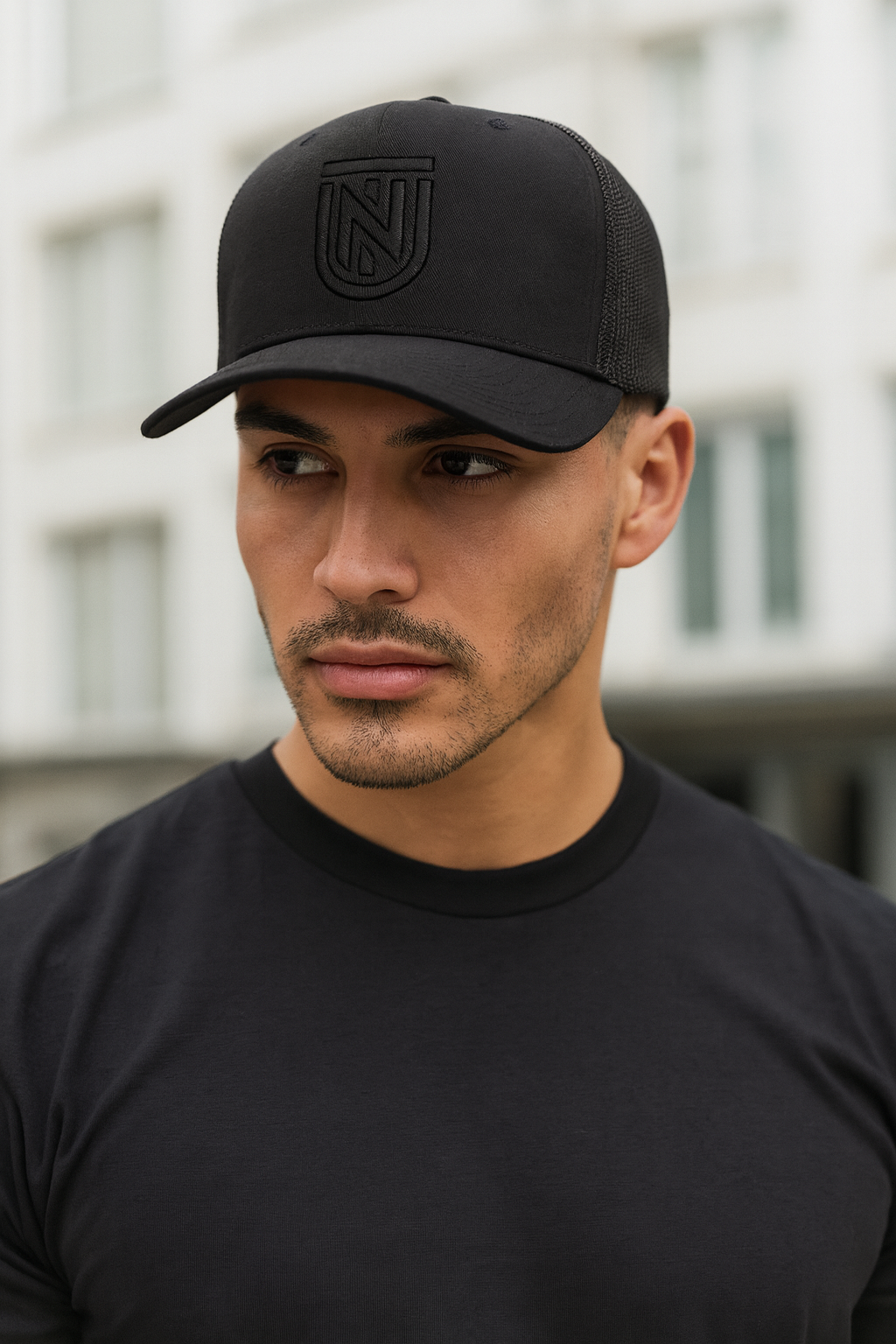 Man wearing a black cap with a logo, looking to the side.